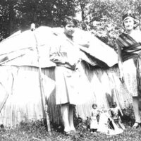 Two young women with wigwam and model tipi with pair of dolls