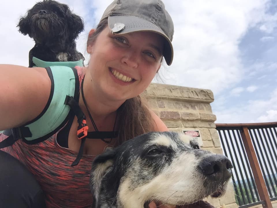 Photo of me with two dogs, one in my backpack and the other in front of me, at a trailhead