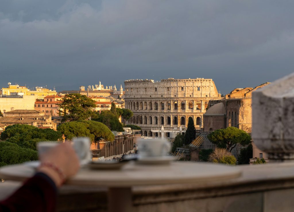 Scenic view of Rome's Colosseum at sunset, framed by a cafe table with coffee cups.